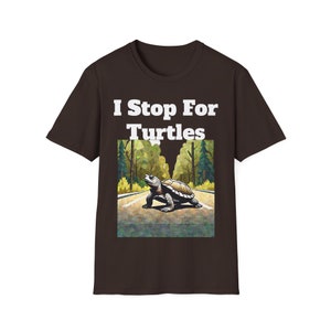 May include: A brown t-shirt with the text "I Stop For Turtles" in white letters. A cartoon turtle is crossing a road in a forest setting.