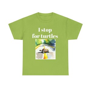 Pode incluir: Uma camiseta verde com o texto "I stop for turtles" impresso em branco. Abaixo do texto, há uma ilustração em aquarela de uma tartaruga cruzando uma estrada.