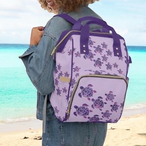 May include: Purple backpack with a sea turtle pattern. The backpack has a zippered front pocket and adjustable straps.