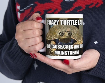 Może przedstawiać: Biały kubek ceramiczny z obrazkiem żółwia w okularach i niebieskiej koszuli. Tekst na kubku brzmi "Crazy Turtle Lady because cats are too mainstream."