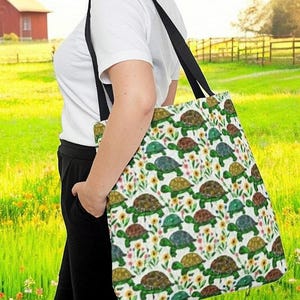 Pode incluir: Uma bolsa tote branca com um padrão colorido de tartarugas e flores. A bolsa tem alças pretas e está sendo segurada por uma pessoa.