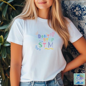 Pu&ograve; includere: Maglietta bianca con una grafica colorata che dice "Don't Stop the STM" in un font divertente.