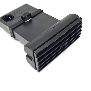 以下が含まれることがあります： 黒色のプラスチック製の車のエアベントで、表面はテクスチャ加工されており、右側に小さなノブがあります。ベントは長方形で、車のダッシュボードにフィットするように設計されています。