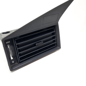 May include: Black plastic car air vent with a horizontal slatted grille and a control knob. The vent has a flap that can be opened and closed.