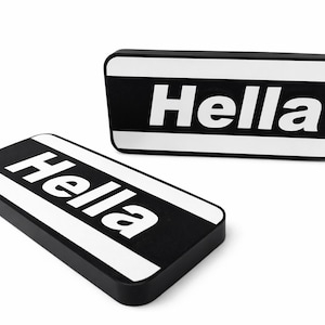 Pode incluir: Dois objetos retangulares em preto e branco com a palavra "Hella" em letras brancas em negrito. Os objetos têm cantos arredondados e uma faixa branca ao longo das bordas superior e inferior. Em um fundo branco.