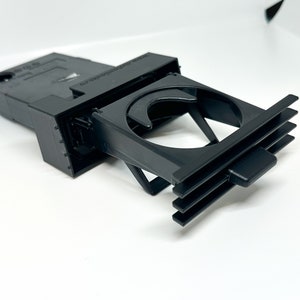 May include: Black plastic car cup holder with a spring-loaded mechanism and a vent clip. The cup holder is designed to fit into a car's air vent.