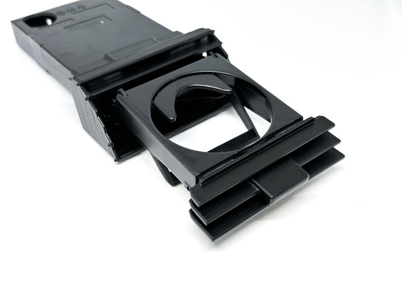 Peut inclure: Porte-gobelet de voiture en plastique noir avec un m&eacute;canisme coulissant. Le porte-gobelet est con&ccedil;u pour s'adapter &agrave; la console centrale d'une voiture.