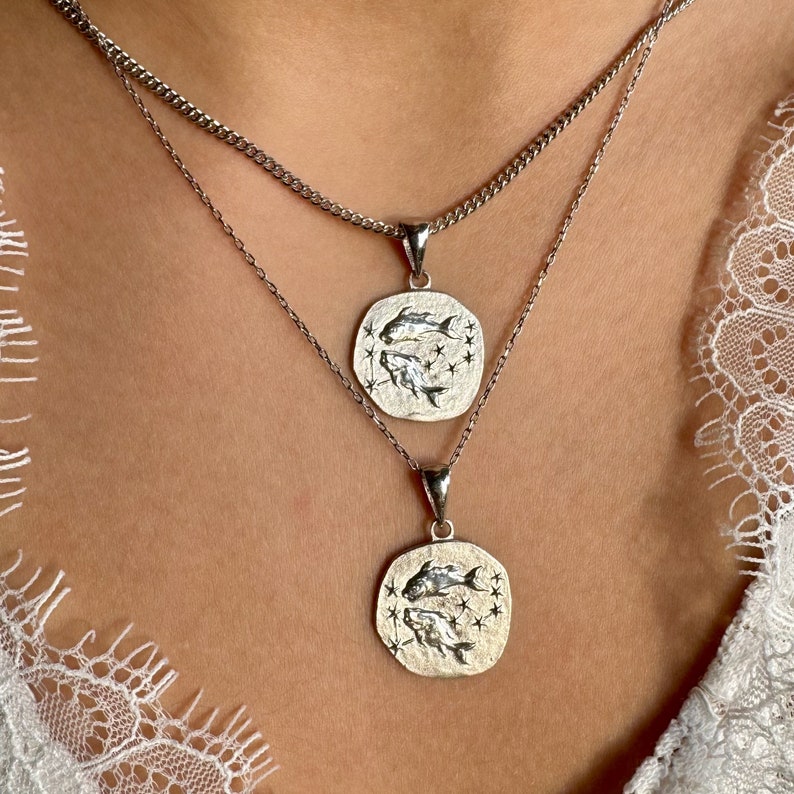 Pisces pendant in the shape of a coin hanging around the neck. Silver color.