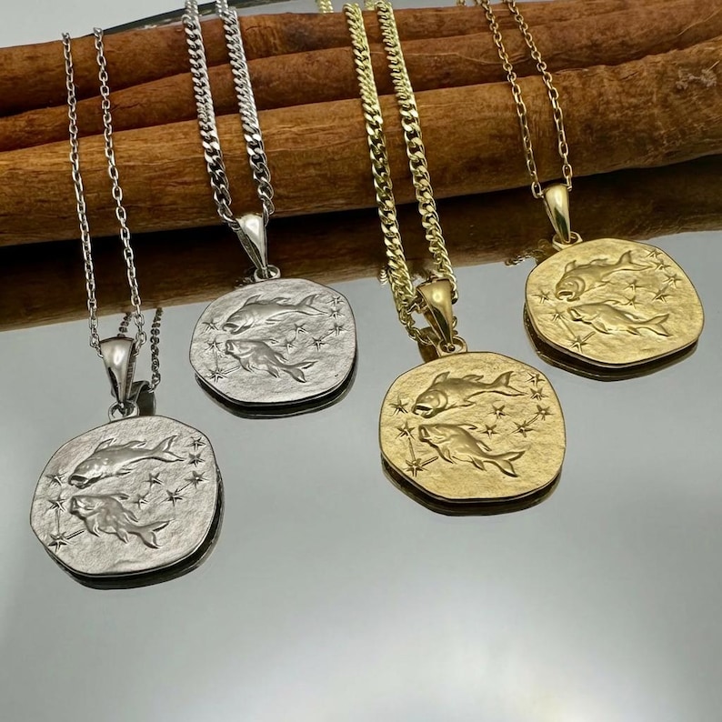Puede incluir: Cuatro collares con colgantes cuadrados con un dise&ntilde;o de pez y detalles de estrellas. Dos collares tienen cadenas y colgantes plateados, mientras que los otros dos tienen cadenas y colgantes dorados. Los colgantes miden aproximadamente 2,5 cm cuadrados.