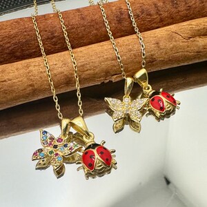 Puede incluir: Tres collares de oro con diferentes colgantes. Un collar tiene un colgante de mariquita, otro tiene un colgante de mariposa con piedras transparentes y el tercero tiene un colgante de flor con piedras de colores.