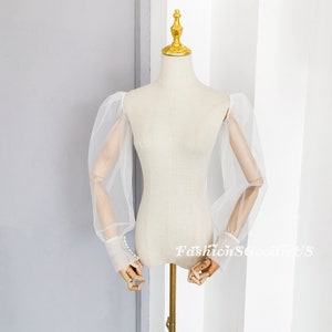 May include: White sheer tulle sleeves with puffed shoulders and pearl button detailing at the cuffs.