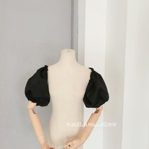 May include: Black off-the-shoulder top with puffy sleeves. The top is made of a smooth, silky fabric.