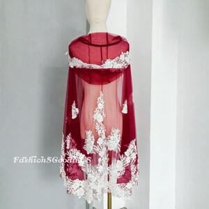 Pode incluir: Capa de noiva de renda transparente bord&ocirc; com bordado floral branco. A capa tem capuz e &eacute; feita de um tecido macio e delicado.