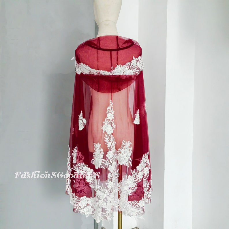 Pode incluir: Capa de noiva de renda transparente bord&ocirc; com bordado floral branco. A capa tem capuz e &eacute; feita de um tecido macio e delicado.