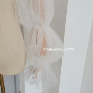 May include: White tulle fabric sleeves with a gathered ruffle detail at the wrist. The sleeves are sheer and delicate, and would be perfect for a wedding or other special occasion.