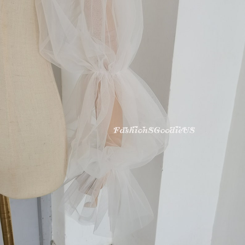 May include: White tulle fabric sleeves with a gathered ruffle detail at the wrist. The sleeves are sheer and delicate, and would be perfect for a wedding or other special occasion.