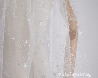 May include: White tulle fabric with silver glitter stars. The fabric is sheer and delicate, perfect for crafting or adding a touch of sparkle to any project.