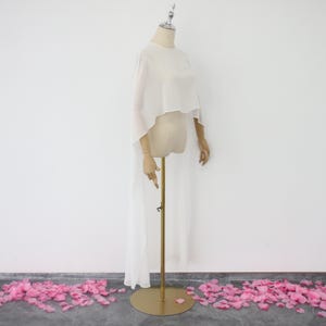 May include: White sheer chiffon cape with a high neckline and long sleeves. The cape is draped over a mannequin and has a long train.