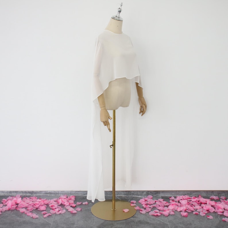 May include: White sheer chiffon cape with a high neckline and long sleeves. The cape is draped over a mannequin and has a long train.