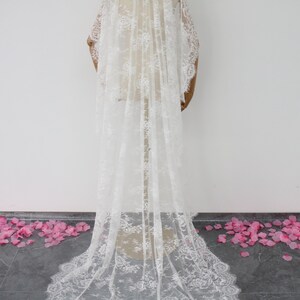 May include: A white lace wedding veil with a delicate floral pattern. The veil is long and flowing, and it is displayed on a mannequin.