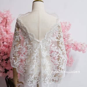 May include: A white lace shawl featuring intricate floral embroidery and a scalloped edge, draped over a mannequin. The sheer fabric displays a delicate pattern of leaves and blossoms. The text FashionSGoodieUS is visible in the lower right corner.