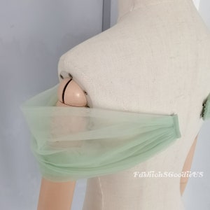 May include: A light green tulle fabric with a gathered edge. The fabric is draped over a dress form's shoulder.