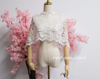 May include: A white lace shawl with floral patterns is displayed on a mannequin. The shawl has a scalloped edge and a delicate, sheer appearance. The mannequin is positioned in front of pink cherry blossom branches.