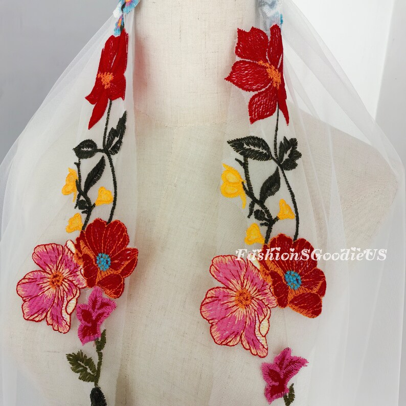May include: White tulle fabric with colourful embroidered flowers. The flowers are red, pink, yellow, and blue. The fabric is sheer and delicate.