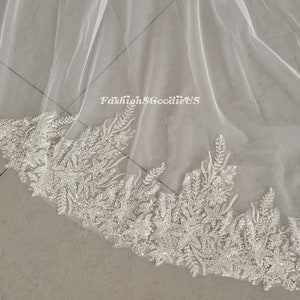 May include: A white tulle wedding veil with a beaded lace trim. The trim features a floral design with small, sparkling beads.