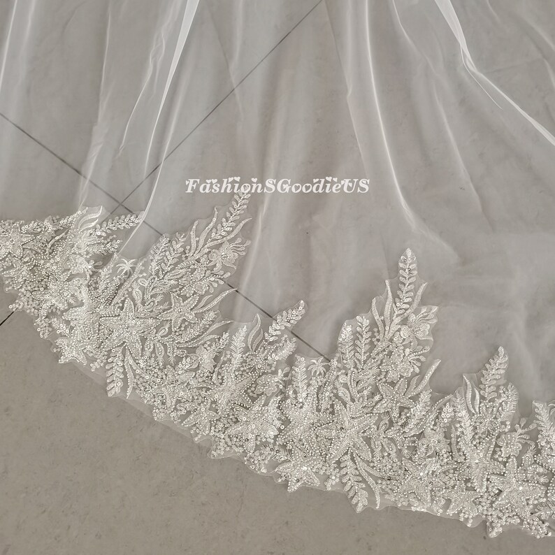 May include: A white tulle wedding veil with a beaded lace trim. The trim features a floral design with small, sparkling beads.