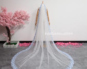 May include: A long, white bridal veil with a delicate, light blue floral trim along the edges. The veil is displayed on a mannequin, showcasing its length and design. The text "FashionSGoodiesUS" is visible on the veil.