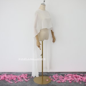 May include: White sheer chiffon cape with a high neckline and a long train. The cape is draped over a mannequin and is displayed against a white background.