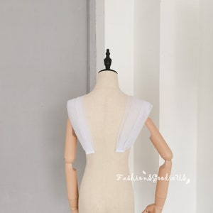 May include: White tulle fabric shoulder straps for a wedding dress or other formal attire. The straps are gathered and layered for a soft, romantic look.