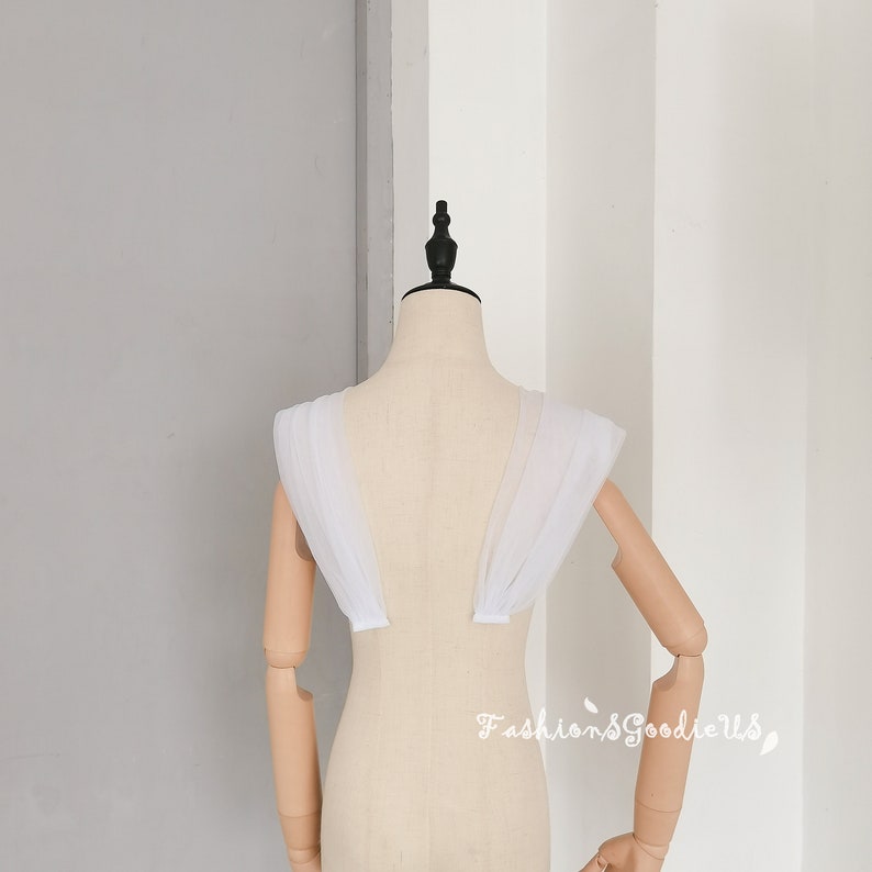 May include: White tulle fabric shoulder straps for a wedding dress or other formal attire. The straps are gathered and layered for a soft, romantic look.