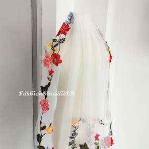 May include: White bridal veil with colourful floral embroidery. The embroidery features red, orange, yellow, pink, blue and green flowers.