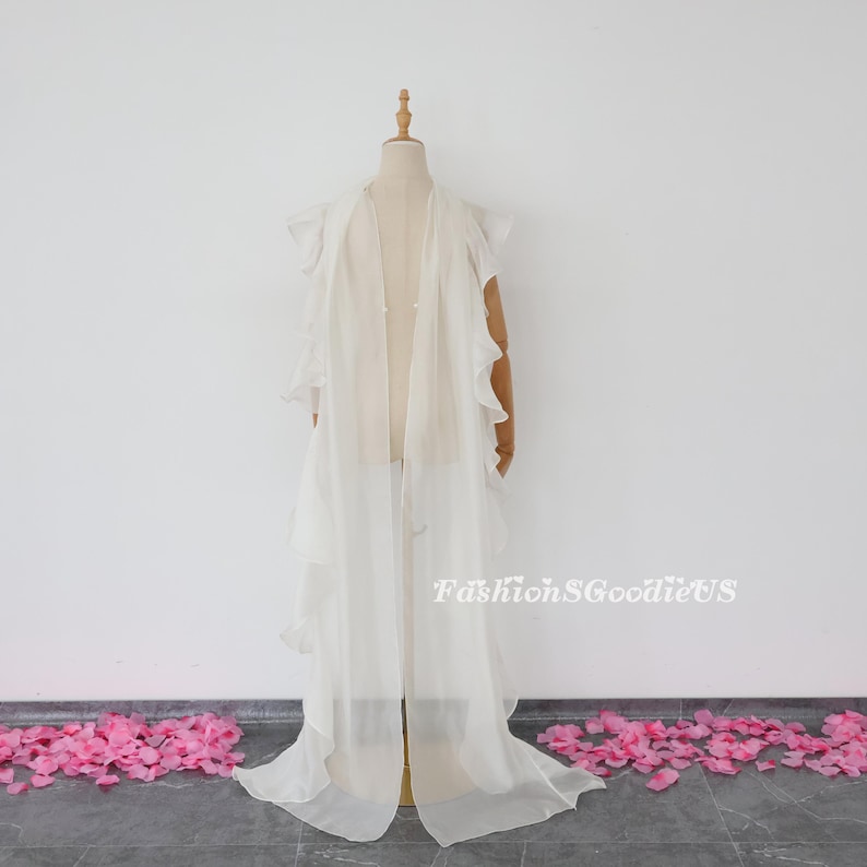 Pu&ograve; includere: Un soprabito bianco in chiffon con bordi arricciati. Il soprabito &egrave; lungo e fluido, ed &egrave; mostrato su un manichino. Il soprabito &egrave; perfetto per aggiungere un tocco di eleganza a qualsiasi outfit.