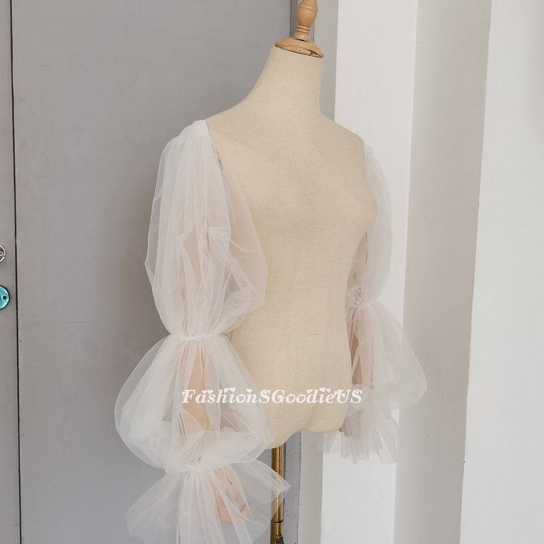 May include: White tulle sleeves with a gathered, puffed design. The sleeves are long and have a delicate, flowing look.