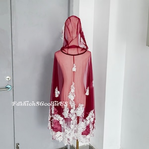 Pode incluir: Capa com capuz de cor bord&ocirc; com acabamento em renda floral branca. A capa &eacute; transparente e tem uma borda de veludo em torno do capuz.