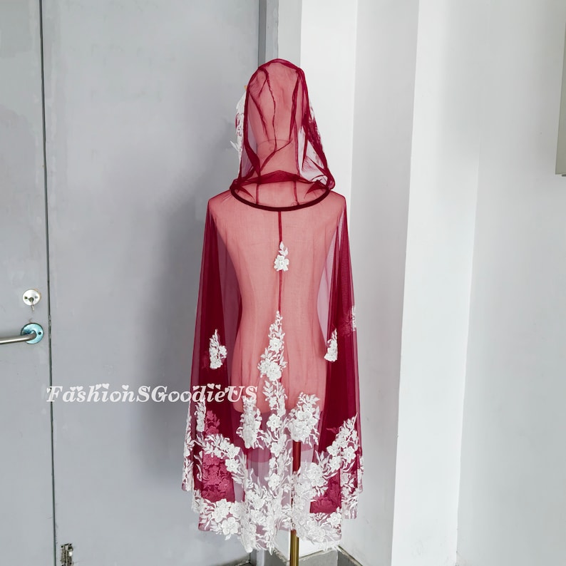 Pode incluir: Capa com capuz de cor bord&ocirc; com acabamento em renda floral branca. A capa &eacute; transparente e tem uma borda de veludo em torno do capuz.