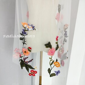 May include: White tulle fabric with colourful embroidered flowers. The flowers are in shades of pink, orange, yellow, blue, and green. The fabric is sheer and delicate.