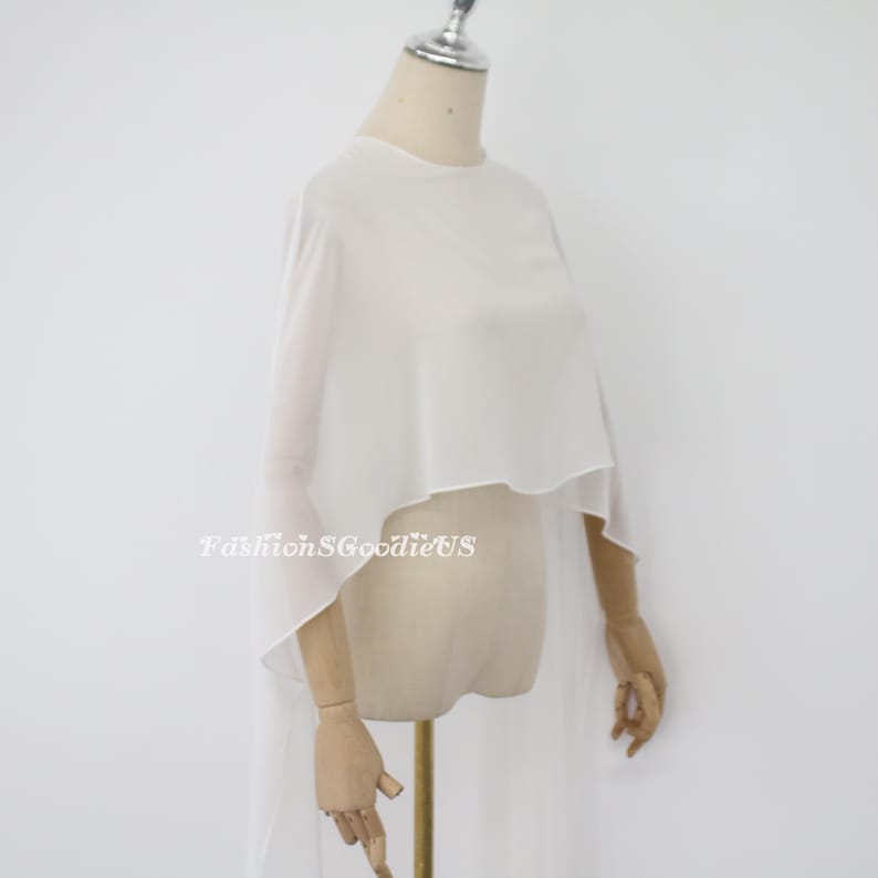 May include: White sheer chiffon cape with a rounded neckline and long flowing sleeves. The cape is draped over a dress form.