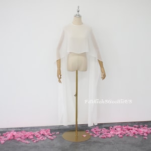 May include: A white sheer cape with a long train, displayed on a mannequin. The cape has a round neckline and is made of a lightweight fabric.