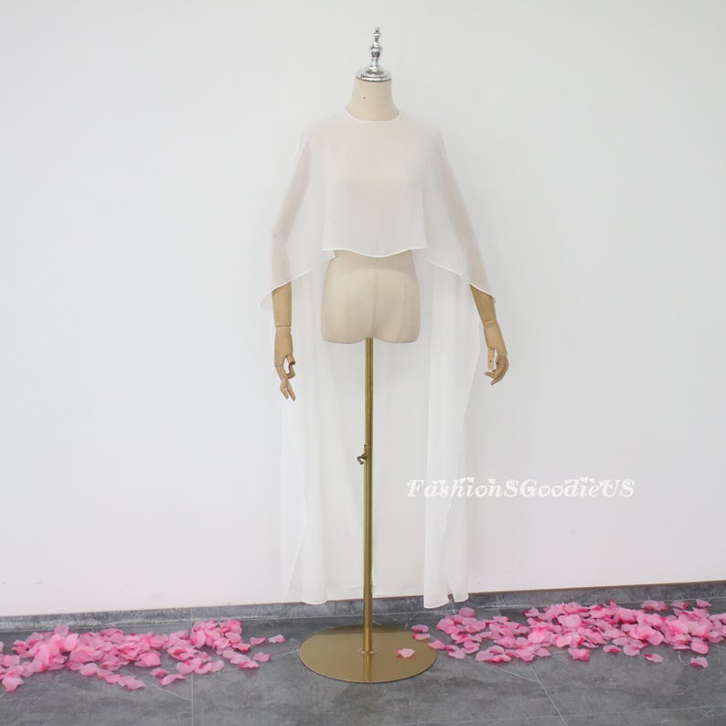 May include: A white sheer cape with a long train, displayed on a mannequin. The cape has a round neckline and is made of a lightweight fabric.