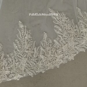 May include: A white tulle bridal veil with a beaded floral lace trim. The lace features a delicate floral design with small, sparkling beads.