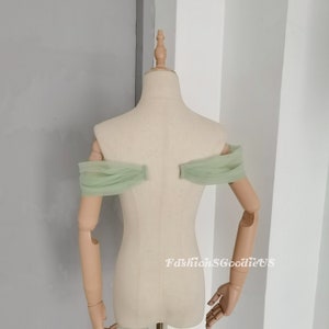 May include: A pair of off-the-shoulder tulle sleeves in a light green color. The sleeves are gathered at the shoulders and have a soft, flowing drape.