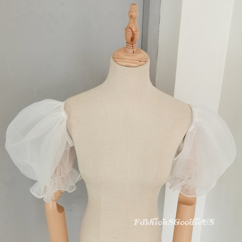 May include: White, sheer, puff sleeves with ruffled cuffs. The sleeves are displayed on a dress form. The text "FashionSGoodieUS" is visible in the lower right corner. The sleeves are made of a lightweight, airy fabric.