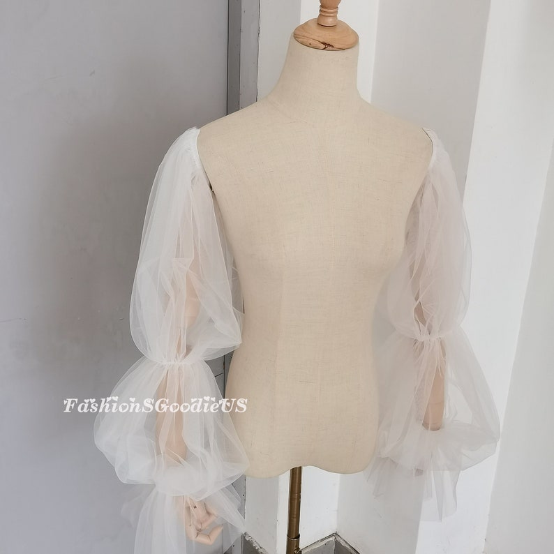 May include: White tulle bridal sleeves with a gathered, puffed design. The sleeves are shown on a white dress form.