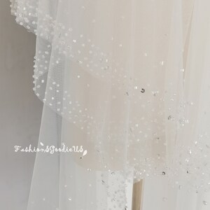 May include: A white bridal veil with a delicate beaded trim. The veil is made of soft tulle and has a flowing, romantic look.