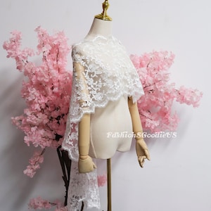 May include: A white lace bridal capelet featuring intricate floral embroidery and a scalloped edge, draped over a mannequin. The fabric is sheer with detailed needlework patterns throughout. The text FashionSGoodieUS is visible on the right side.