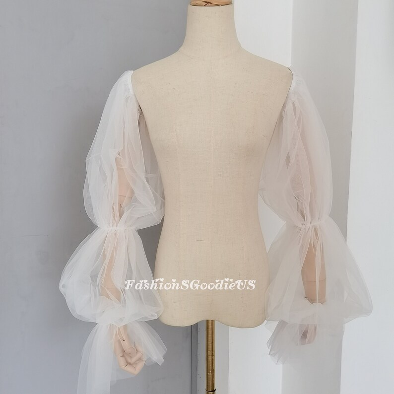 May include: White tulle sleeves with a gathered, puffed design. The sleeves are long and have a gathered cuff at the wrist.